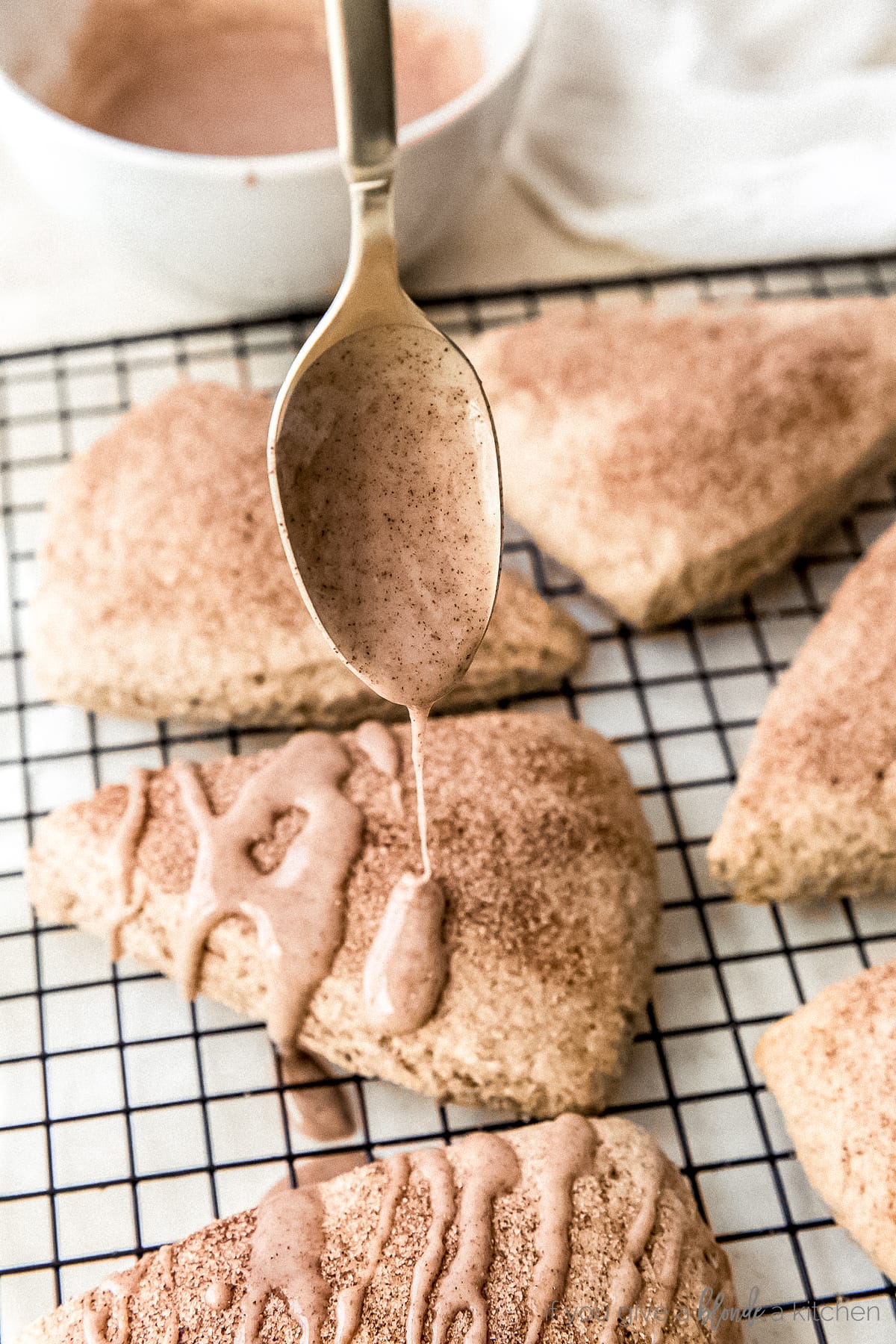 spoon drizzling cinnamon glaze over cinnamon scone on wire cooling rack