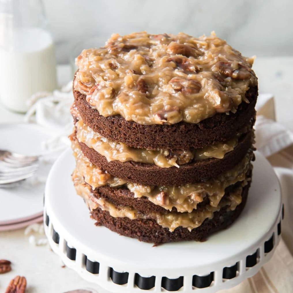 four layer german chocolate cake with coconut pecan filling on white cake stand