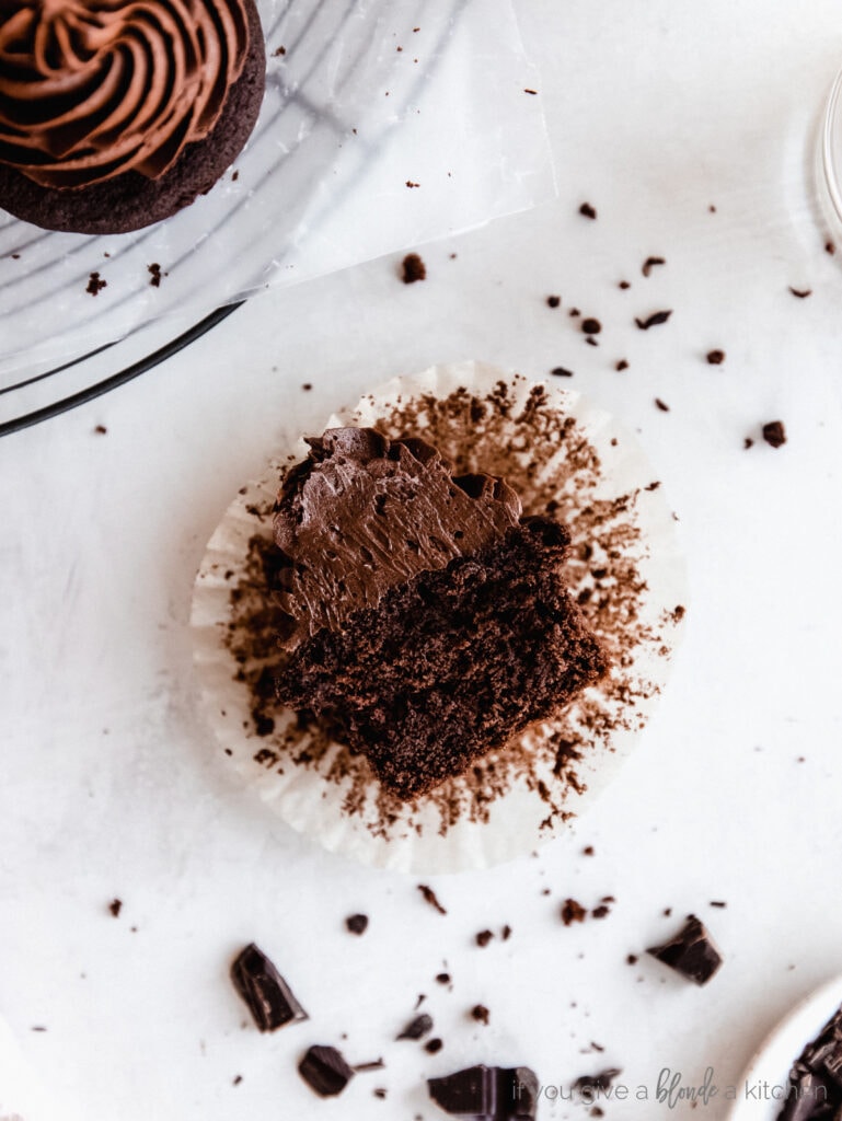 chocolate cupcake with chocolate frosting cut in half on top of paper liner