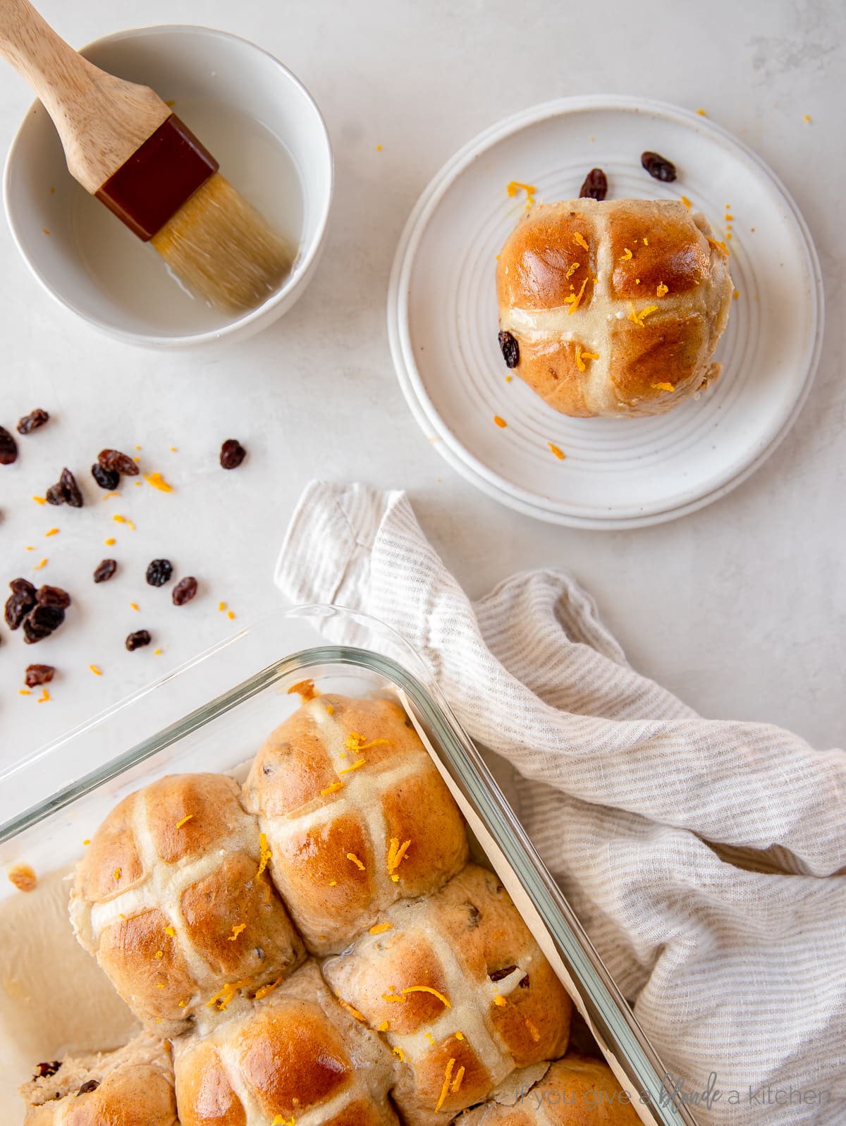 hot cross bun on a small round plate next to baking dish with more buns