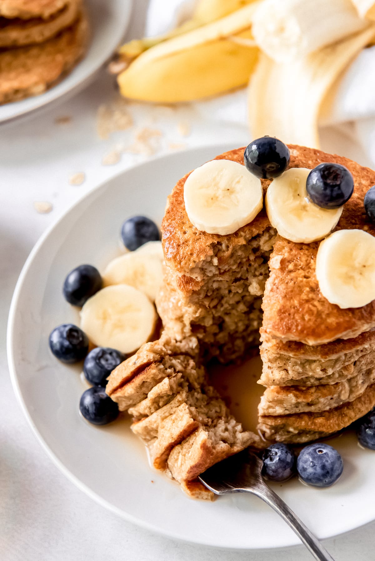 stack of banana oatmeal pancakes on plate with fork holding a bite