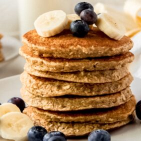 stack of banana oatmeal pancakes on white plate with banana slices and blueberries