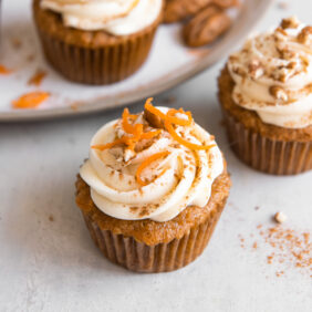 carrot cake cupcake with cream cheese frosting and shredded carrots on top.