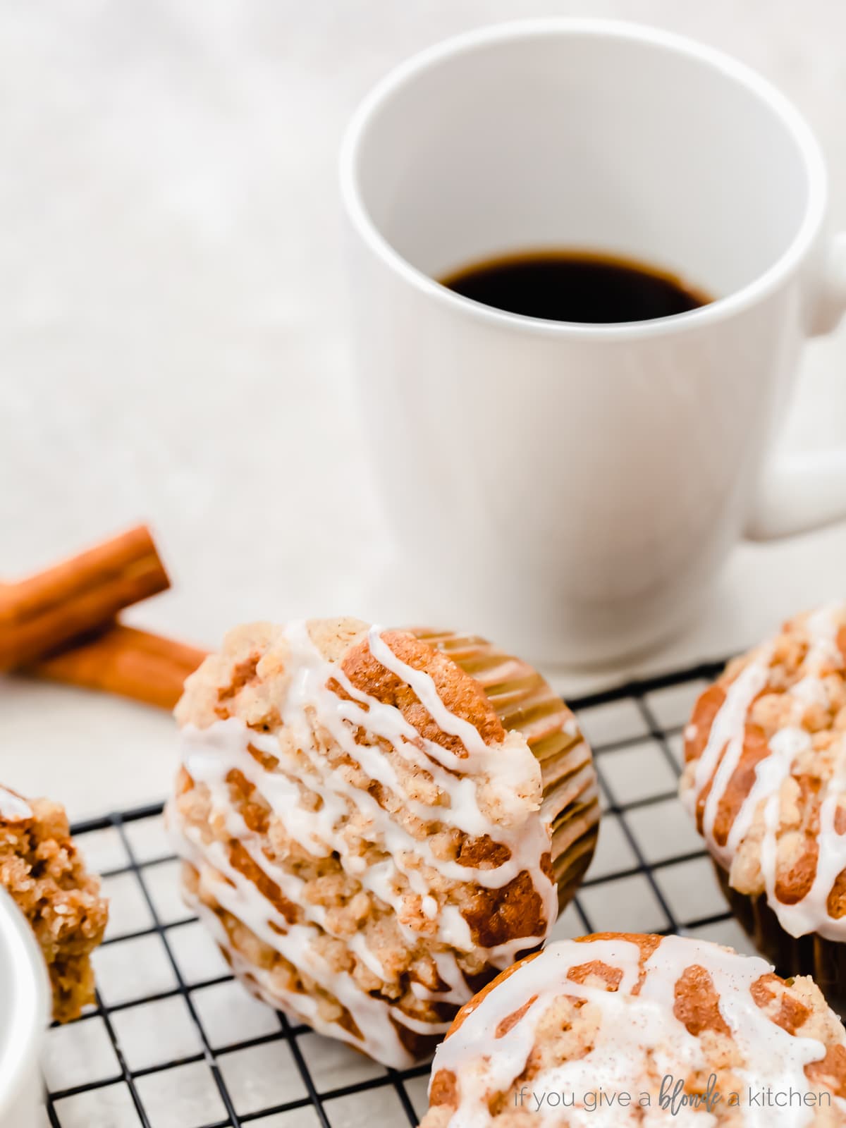 coffee cake muffin with icing turned on its side next to white mug of coffee