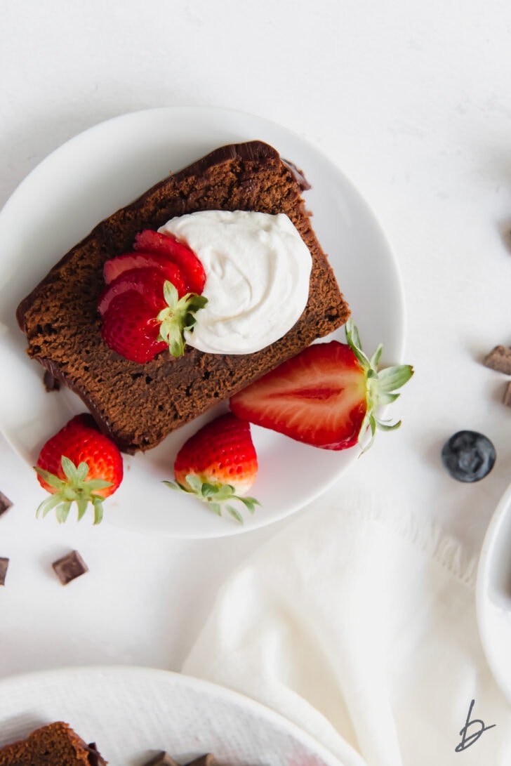 slice of chocolate pound cake on plate with whipped cream and strawberries