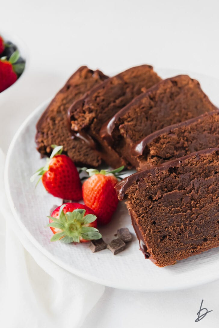 slices of chocolate pound cake on white plate with strawberries