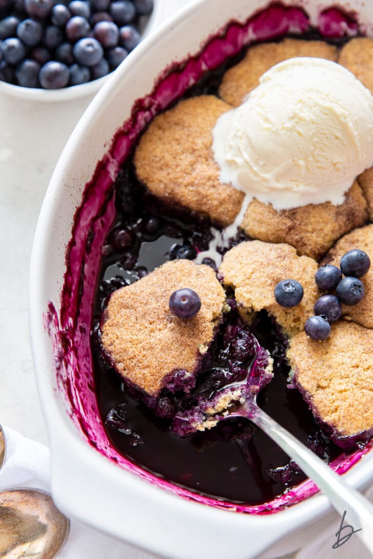 serving spoon with blueberry cobbler in baking dish