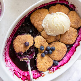 oval baking dish with blueberry cobbler and a scoop of vanilla ice cream