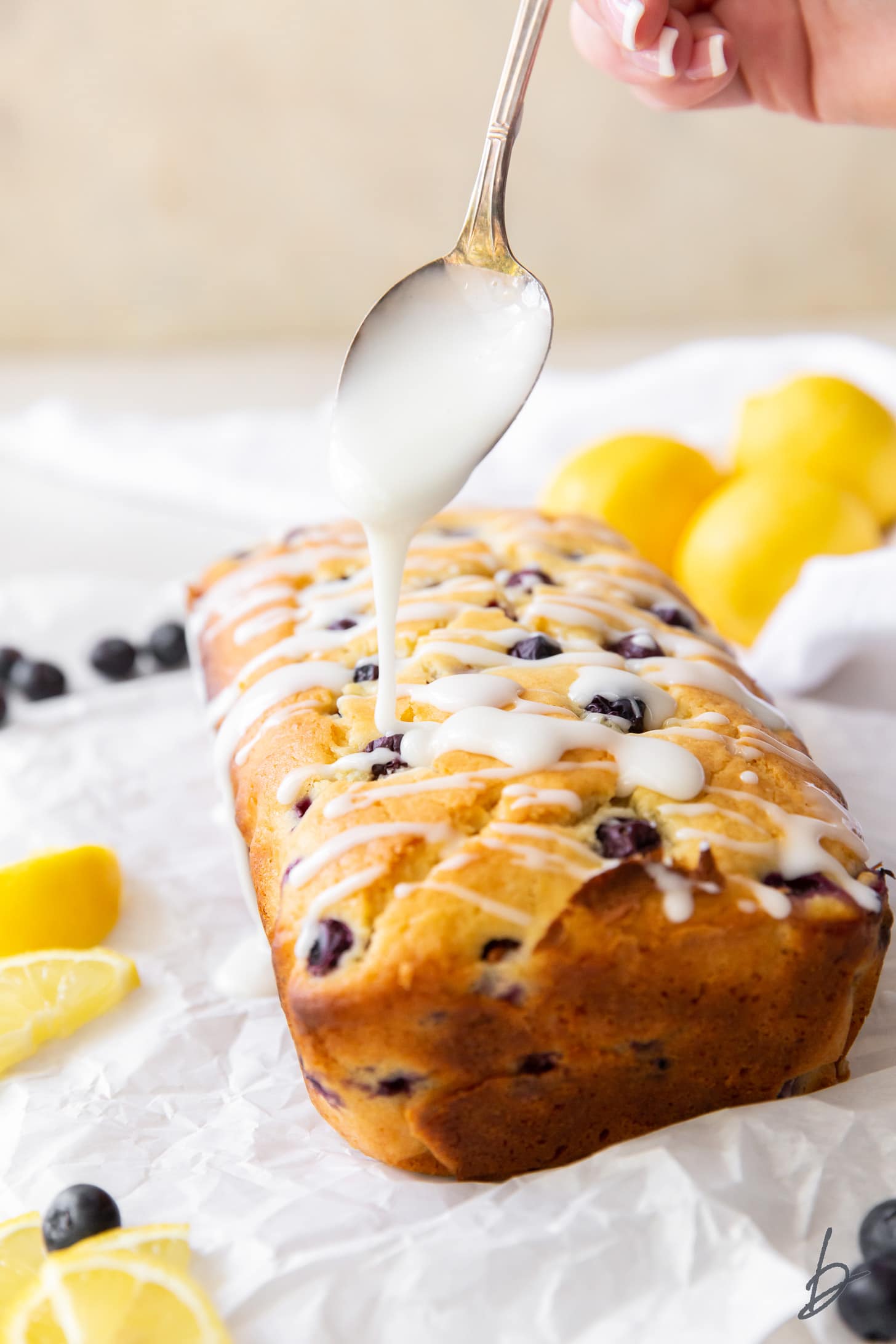 spoon drizzling lemon glaze on top of lemon blueberry loaf.