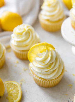 lemon cupcake with lemon buttercream frosting and a lemon slice next to another lemon slice and cupcake.