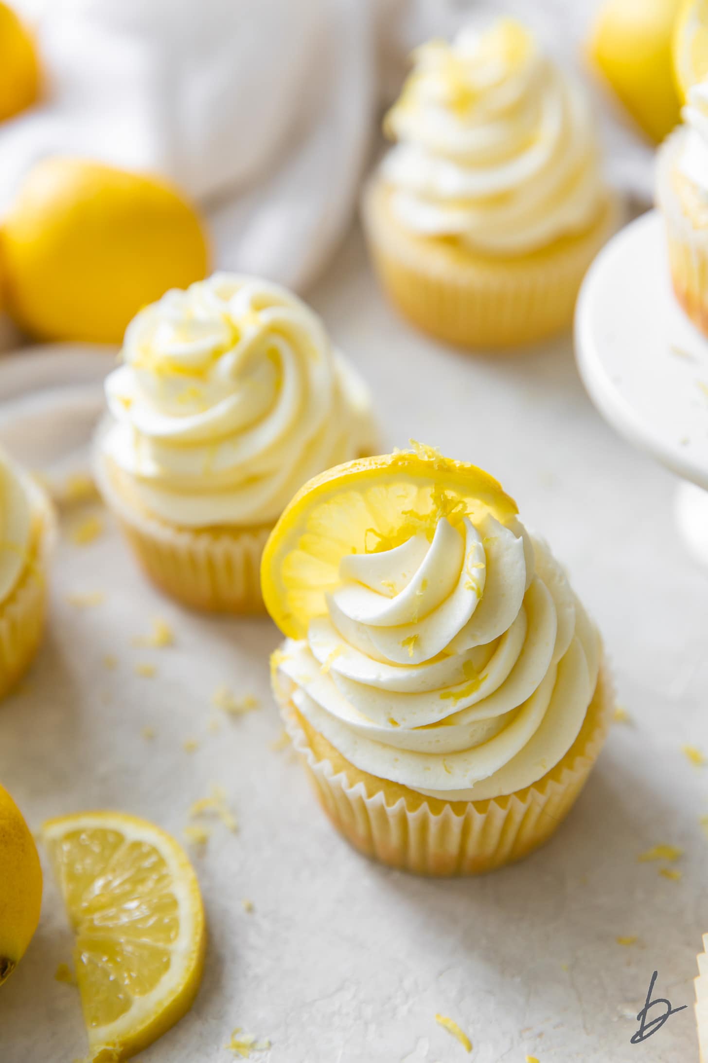 lemon cupcake with lemon buttercream frosting and a lemon slice next to another lemon slice and cupcake.