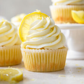 lemon cupcake topped with lemon buttercream frosting and a lemon slice next to more cupcakes and a lemon