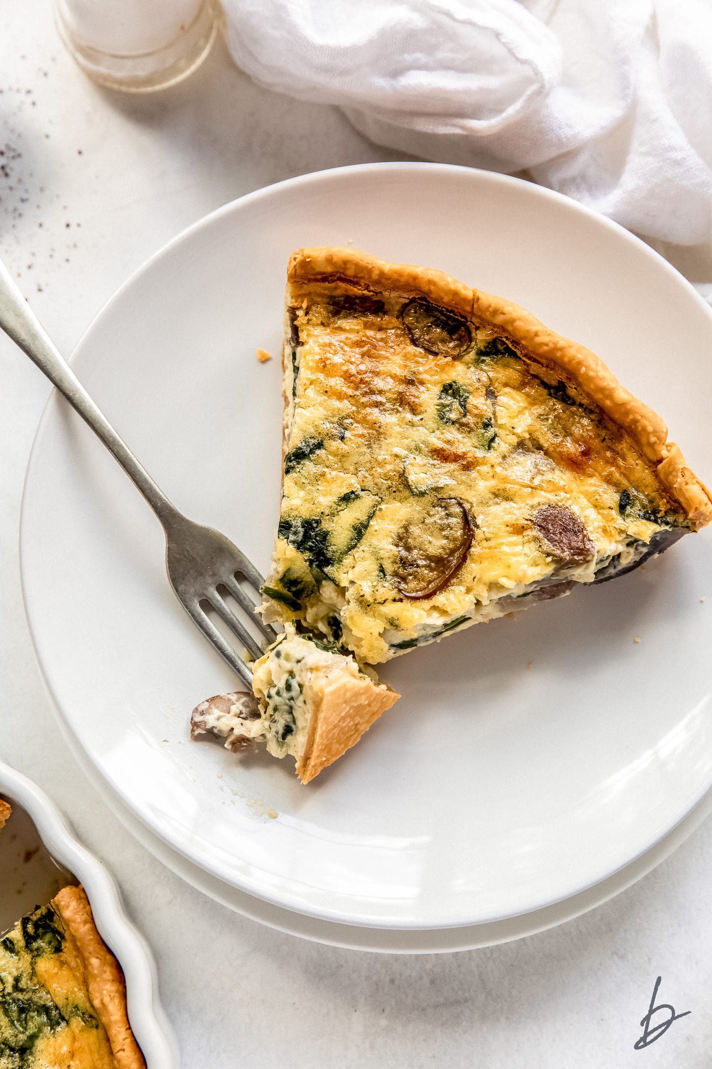 slice of spinach mushroom quiche ona plate with fork taking a bite