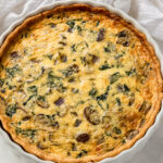 spinach mushroom quiche in a white ceramic quiche dish