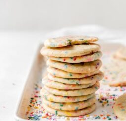 tall stack of sprinkle sugar cookies on a cookie sheet with more sprinkles