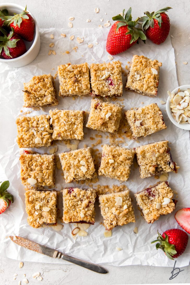 strawberry oatmeal bars cut into squares on parchment paper next to fresh strawberries