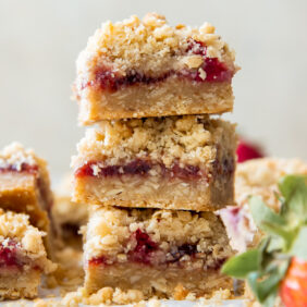 stack of three strawberry oatmeal bars next to a fresh strawberry