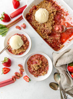 strawberry rhubarb crisp in baking dish and two bowls, one bowl with ice cream