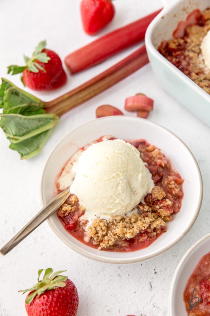 bowl of strawberry rhubarb crisp with scoop of vanilla ice cream and spoon