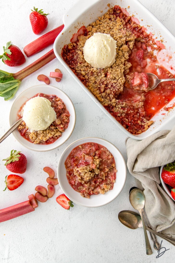 strawberry rhubarb crisp in baking dish and two bowls, one bowl with ice cream