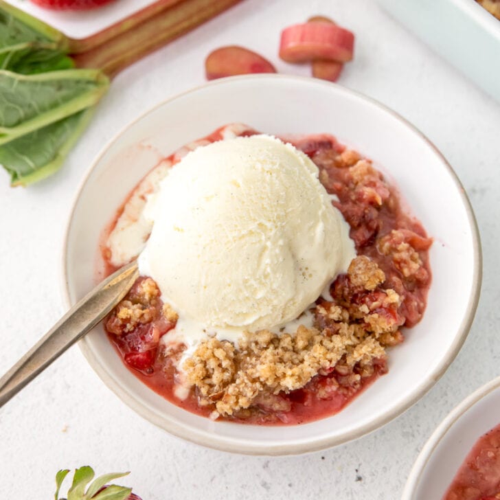 bowl of strawberry rhubarb crisp with a big scoop of vanilla ice cream on top