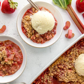 two bowls with strawberry rhubarb crisp, one bowl with scoop of vanilla ice cream on top of crisp