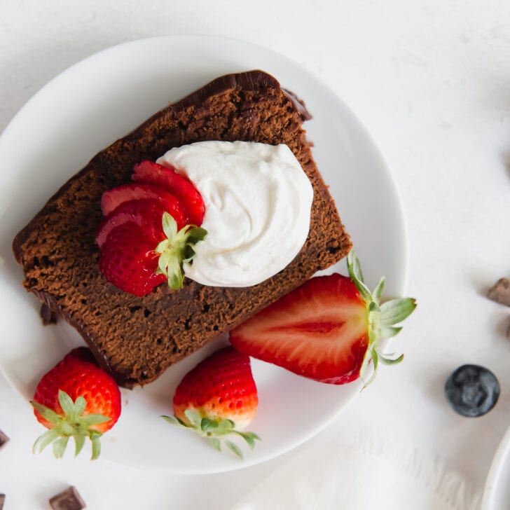 white round plate with slice of chocolate pound cake with whipped cream and strawberries