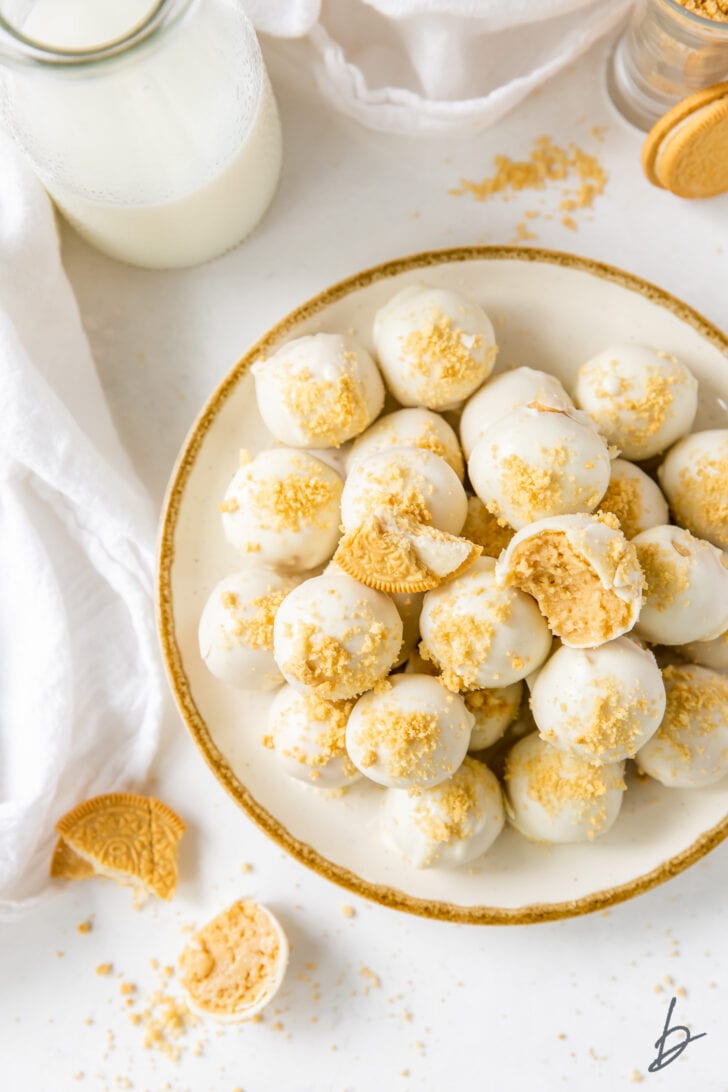 white chocolate covered golden oreo truffles on gold rimmed white plate next to glass bottle of milk