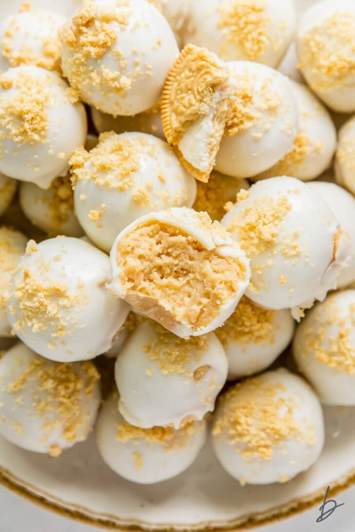golden oreo truffle with a bite on top of pile of more white chocolate covered golden oreo truffles