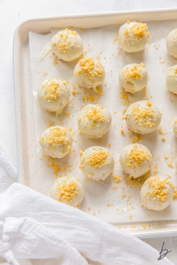 parchment-lined baking sheet with golden oreo truffles with white chocolate and cookie crumbs on top