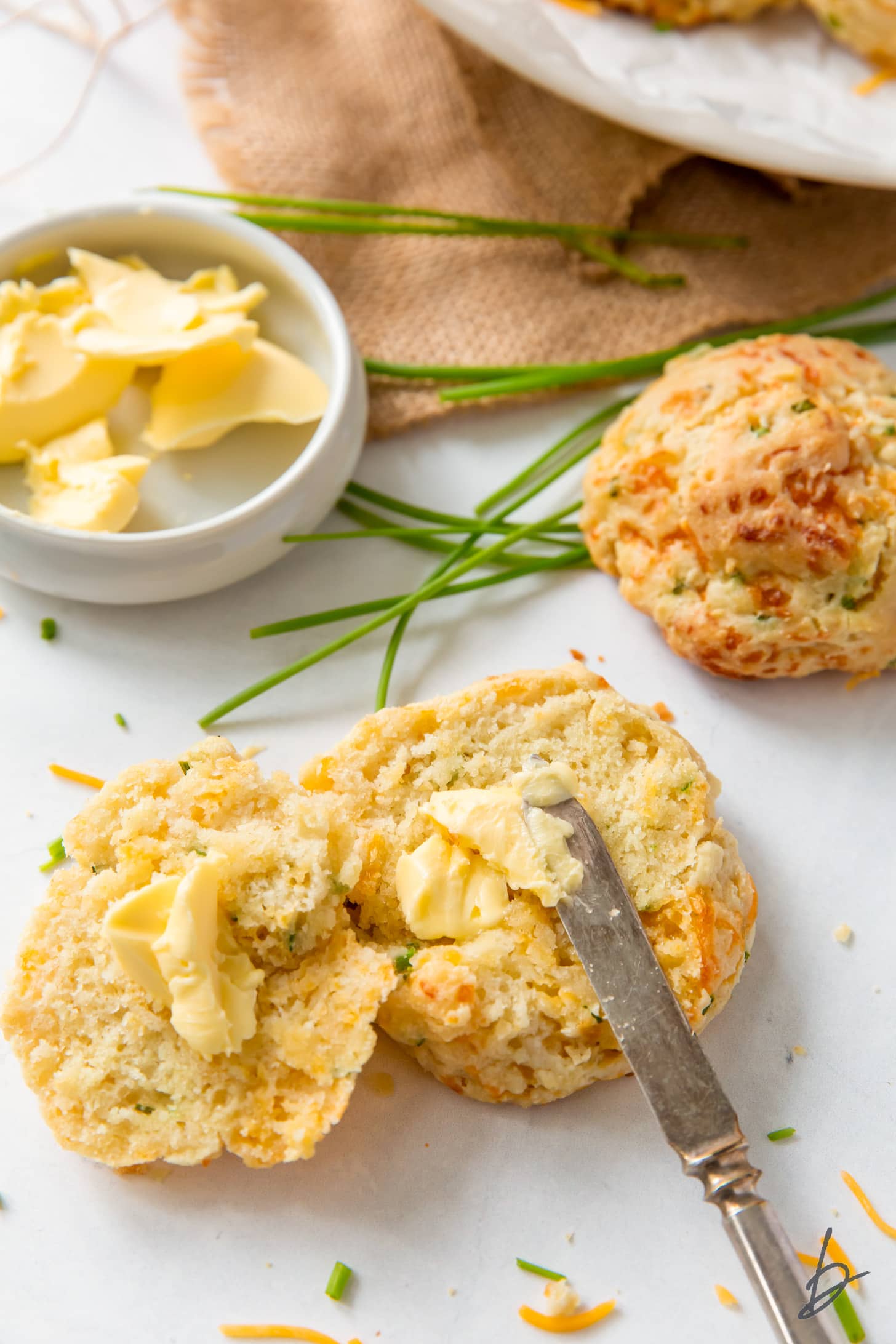 knife spreading butter in the center of a cheddar biscuit cut in half length wise