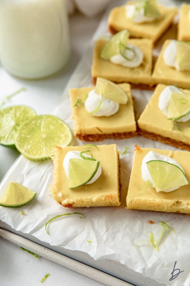 key lime pie bars on crinkled wax paper next to lime slices