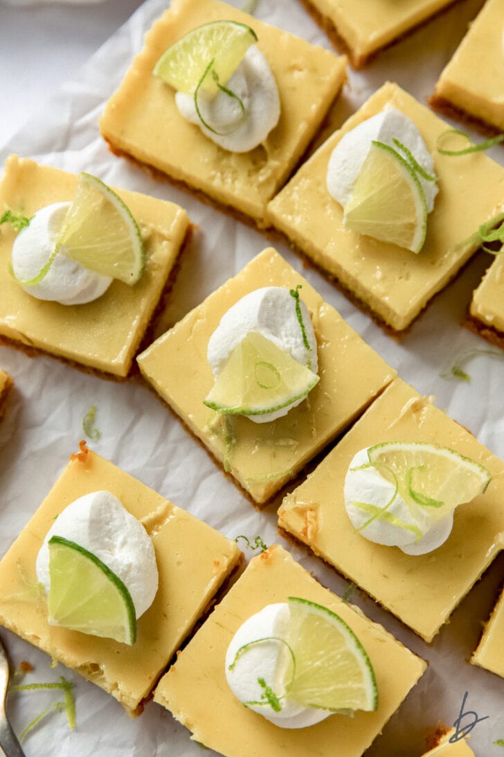 tops of key lime pie bars garnished with whipped cream and lime slices