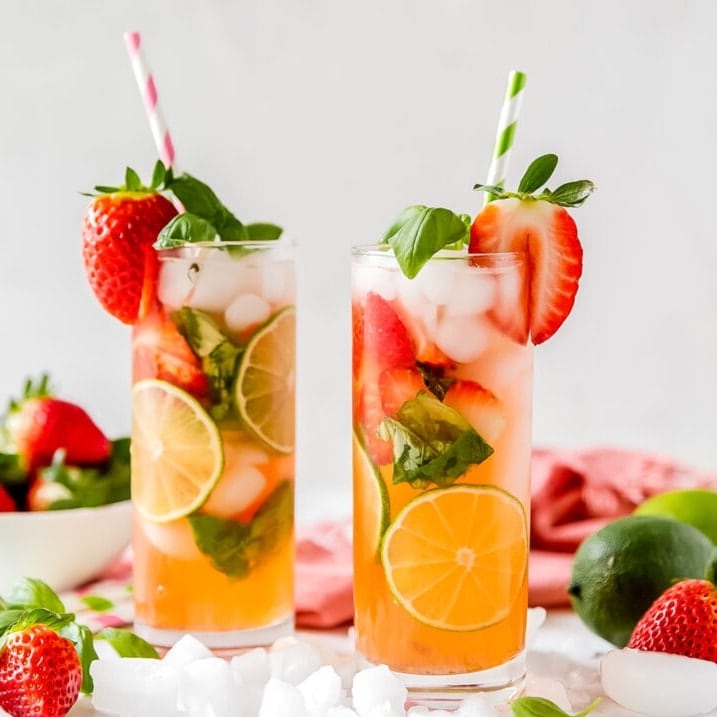 two tall glasses of stawberry mini mojitos garnished with sliced strawberries and striped paper straws