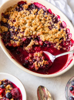 triple berry crisp in an oval baking dish with serving spoon holding some crisp