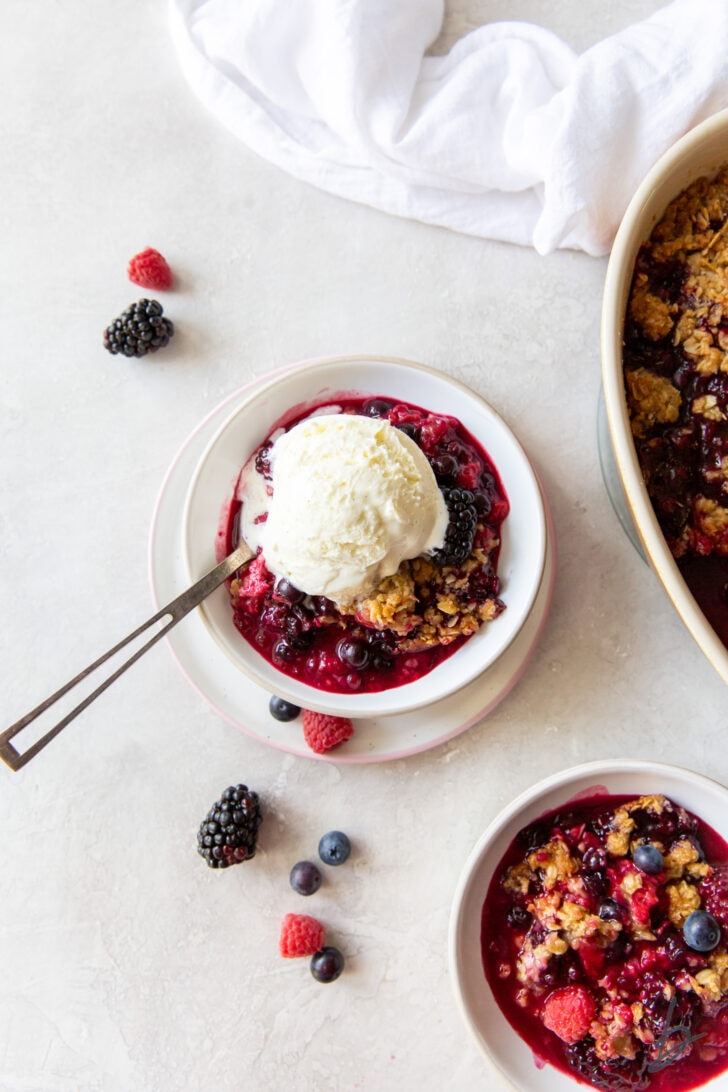 triple berry crisp in a bowl with scoop of vanilla ice cream and spoon