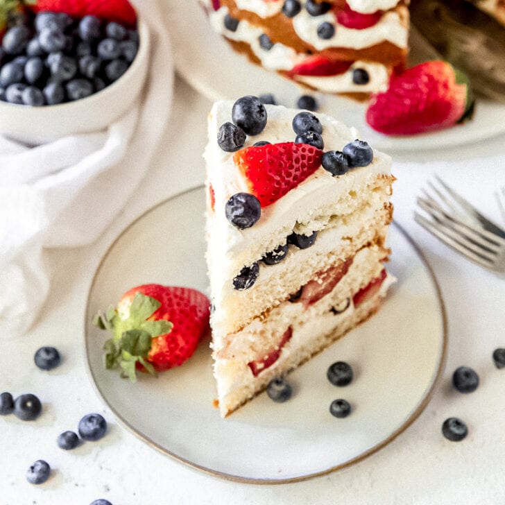 slice of triple berry layer cake on white plate with strawberries and blueberries