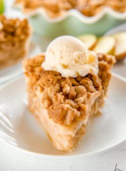 slice of apple crumble pie topped with a scoop of ice cream on a white round plate