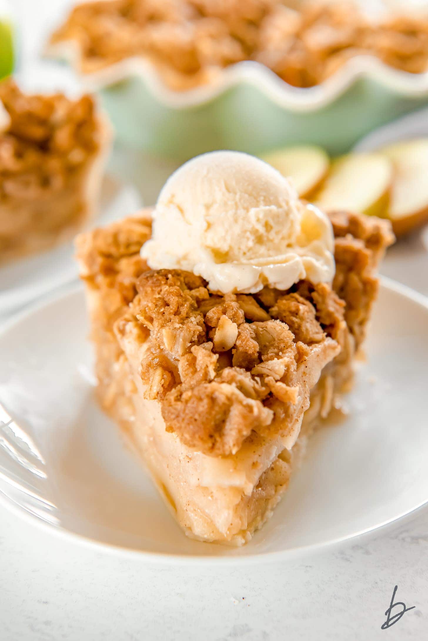 slice of apple crumble pie topped with a scoop of ice cream on a white round plate