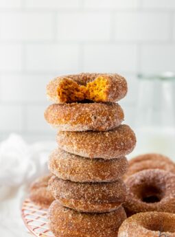 baked pumpkin donuts in a stack with top donut with a bite