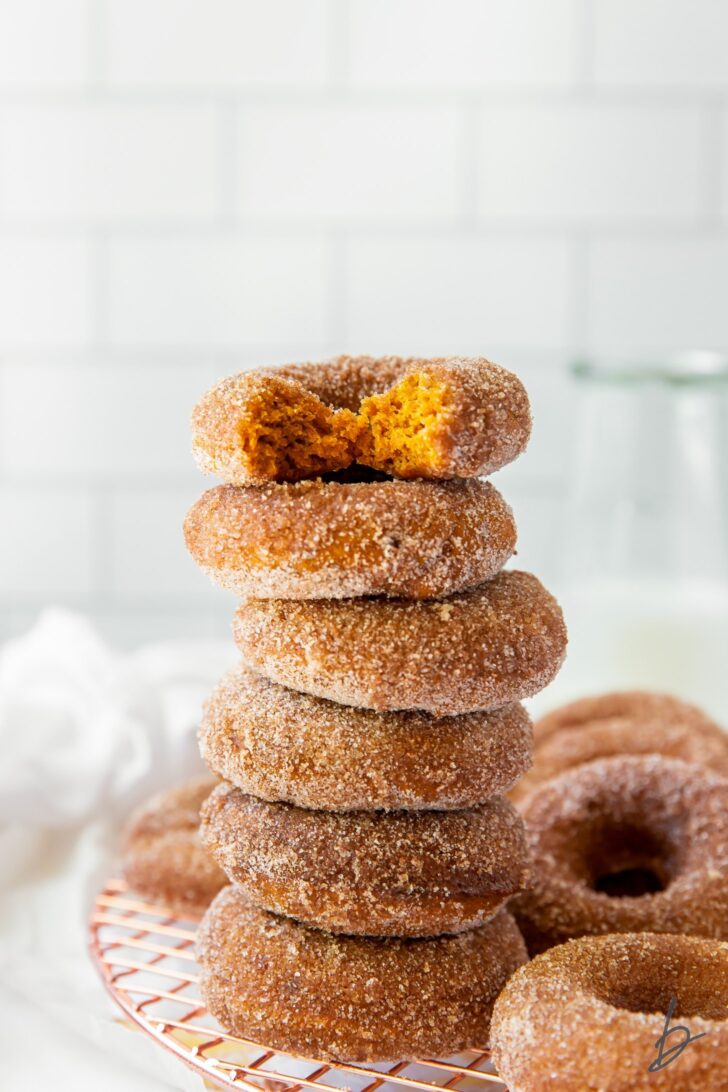 baked pumpkin donuts in a stack with top donut with a bite