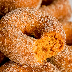 pumpkin donut with a bite taken out on top of pile of more donuts covered in cinnamon sugar