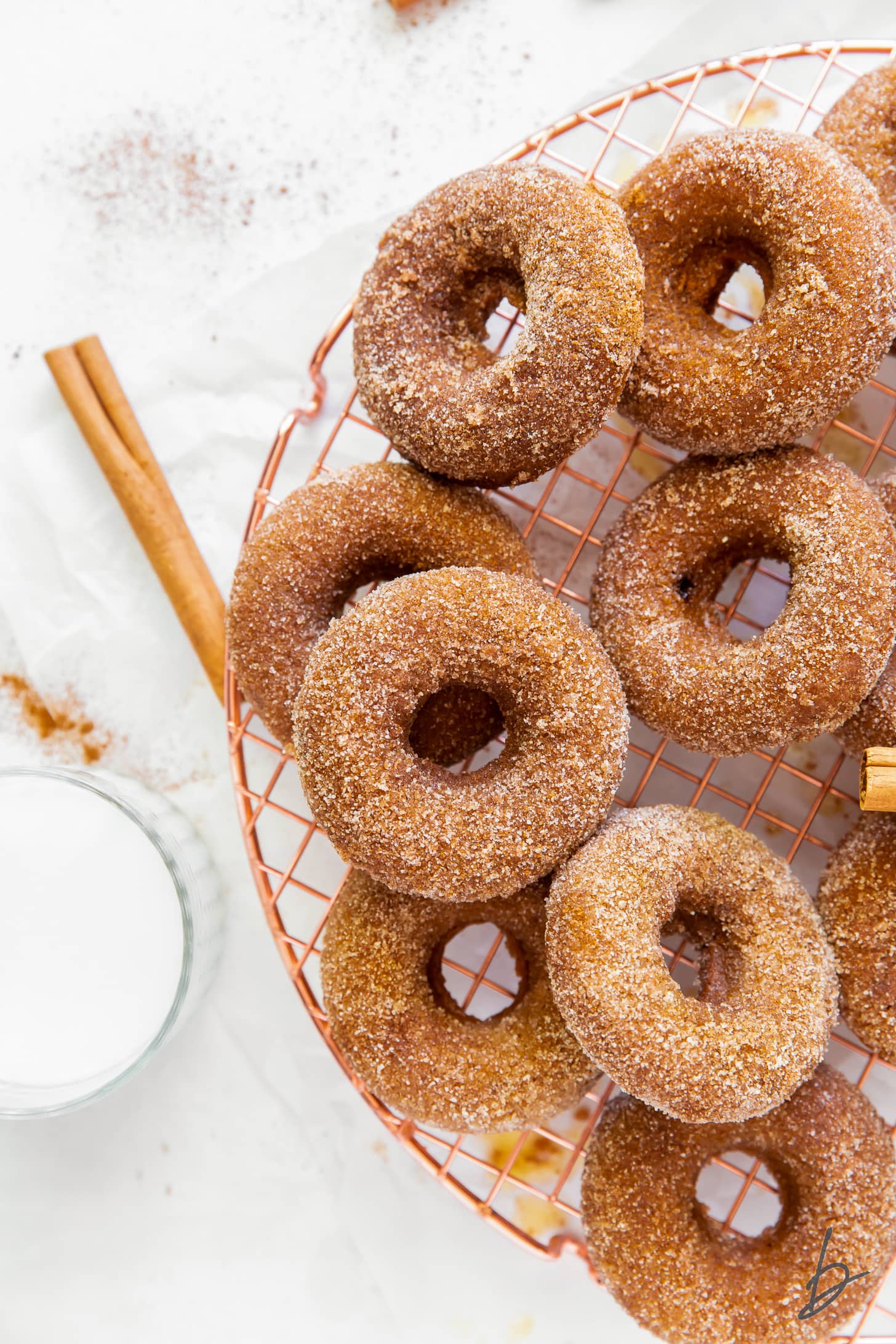 cinnamon sugar coated baked pumpkin donuts on round copper wire cooling rack next to cinnamon stick