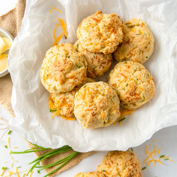 cheddar biscuits in a bowl on crinkled paper next to fresh chives