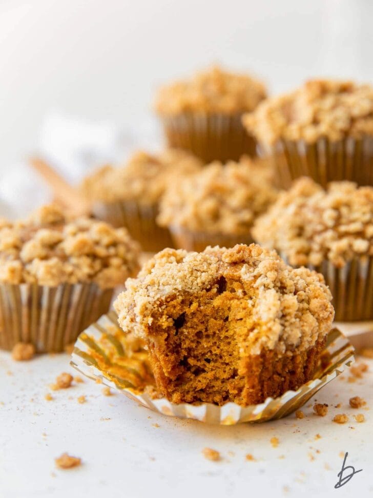 pumpkin muffin with a bite sitting on open paper liner with more muffins behind it