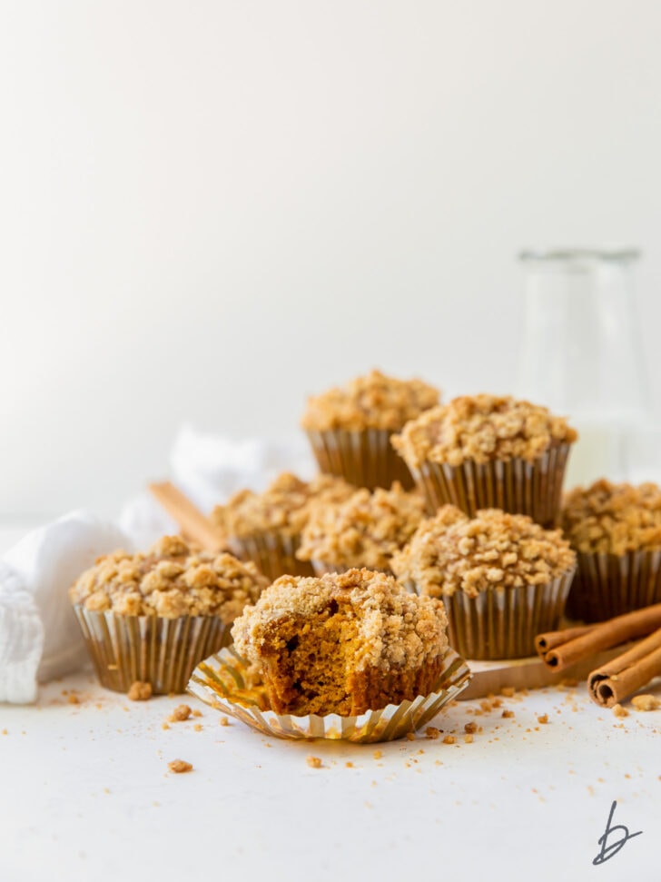 pumpkin muffin with streusel on open paper liner with more muffins piled in the background