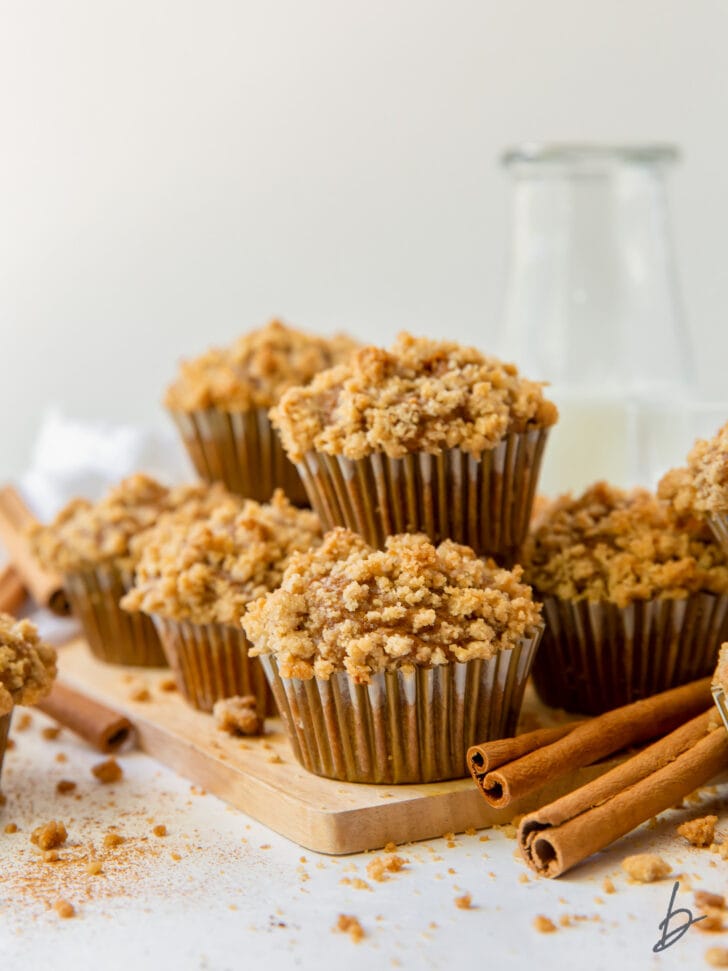 pumpkin muffins with streusel in pile on small wood cutting board next to cinnamon sticks
