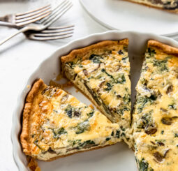 spinach mushroom quiche in a white ceramic quiche dish with two slices cut.