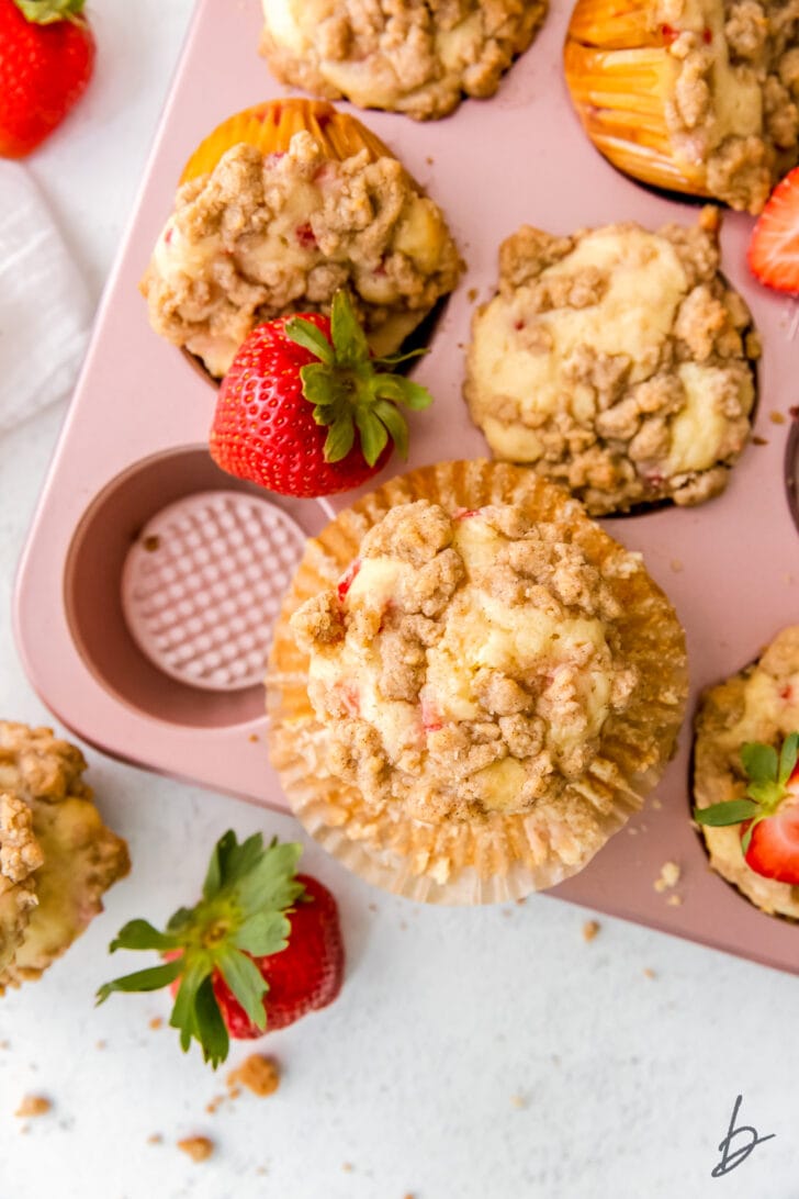 strawberry muffin with streusel on paper liner on top of pink muffin tin with more streusel
