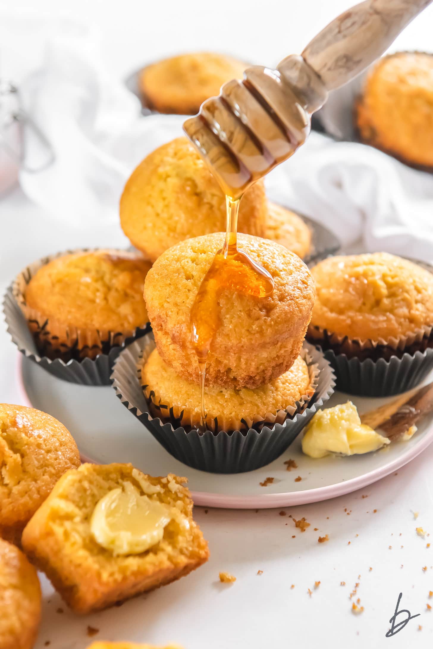 honey being drizzled on top of two cornbread muffins stacked on plate with more muffins